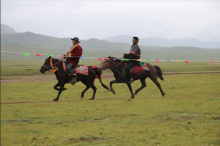 Two men ride horses across the grassland during a horse race event