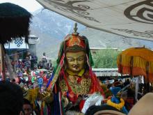 Painted gold image of Guru Rinpoche surrounded by festival goers